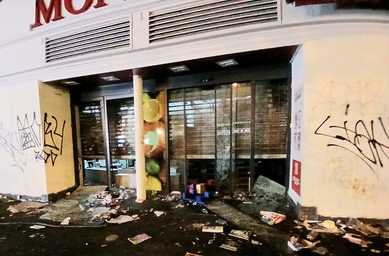 一間遭洗劫的 Monoprix 超市入口，玻璃破碎、地上滿是雜物